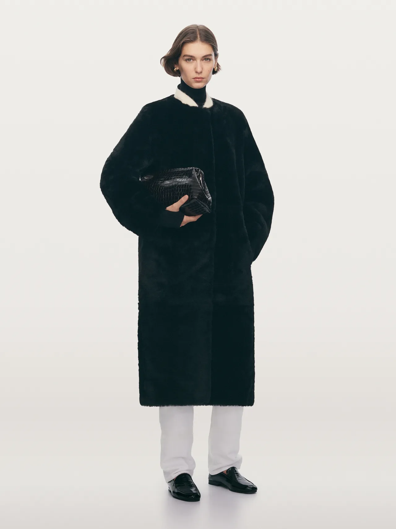 Model in a black faux fur coat holding a clutch bag.