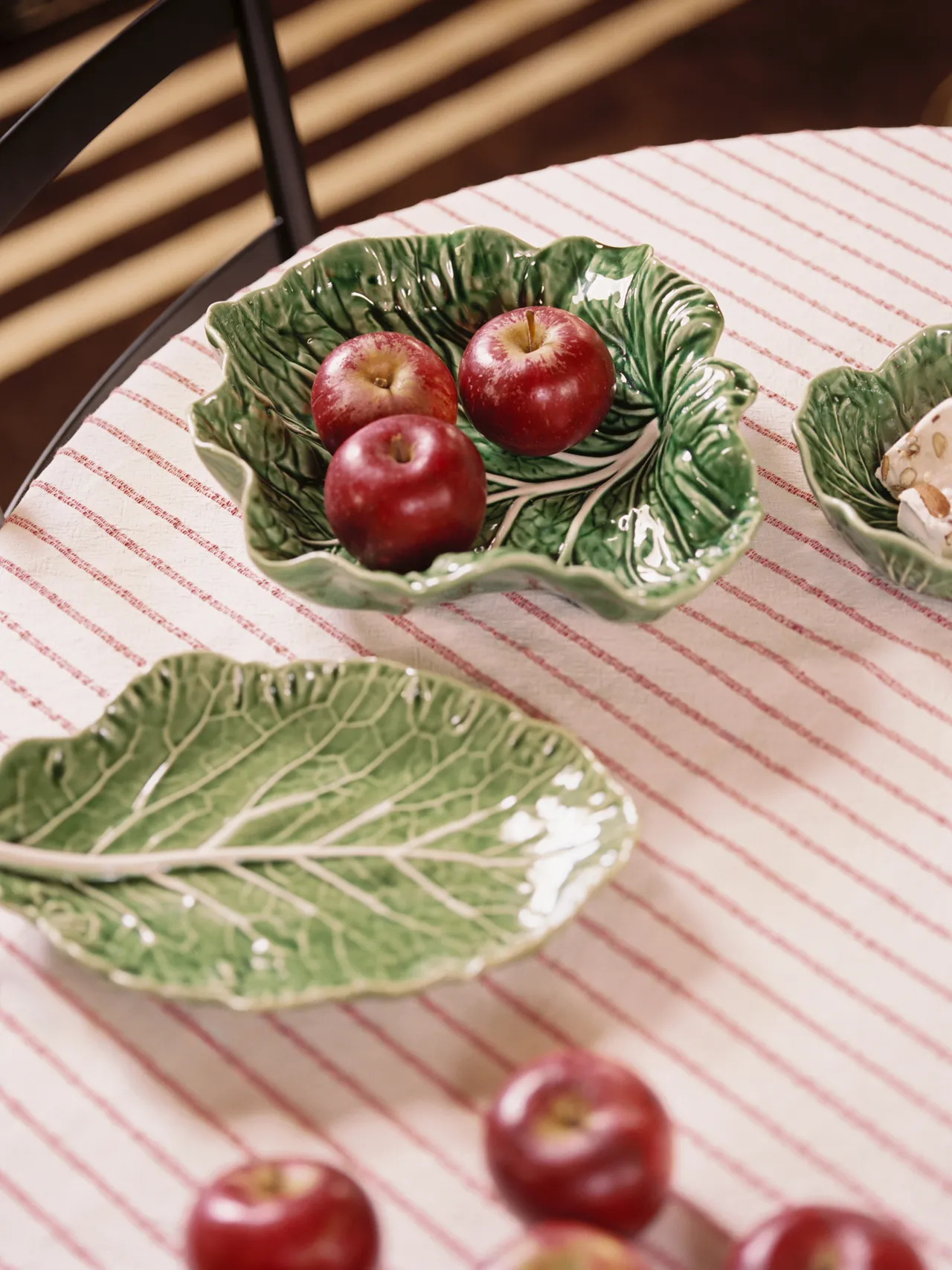 Green ceramic tableware with red apples on a striped tablecloth.