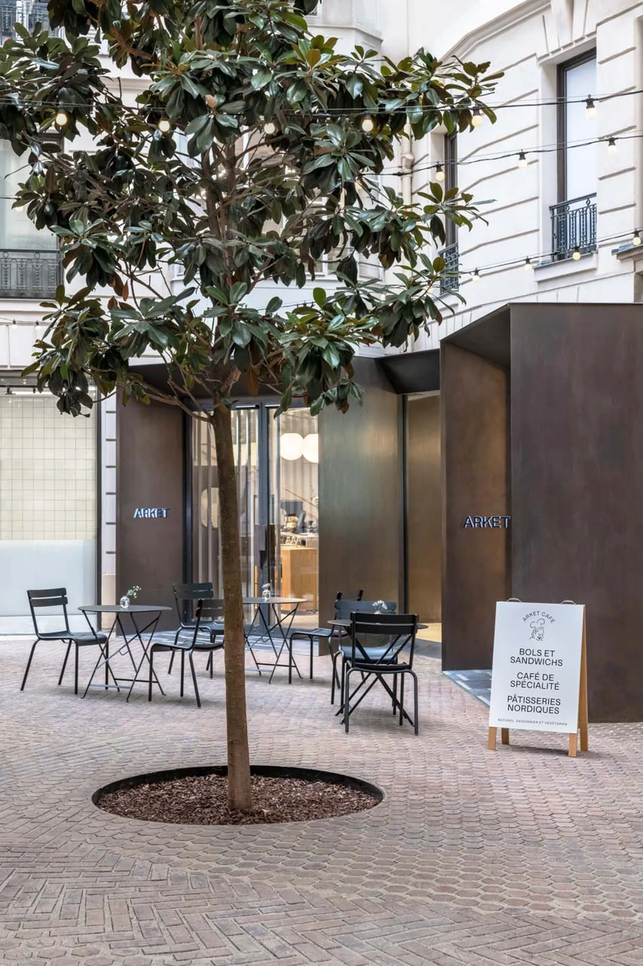 Exterior of an ARKET café with outdoor seating and a tree.