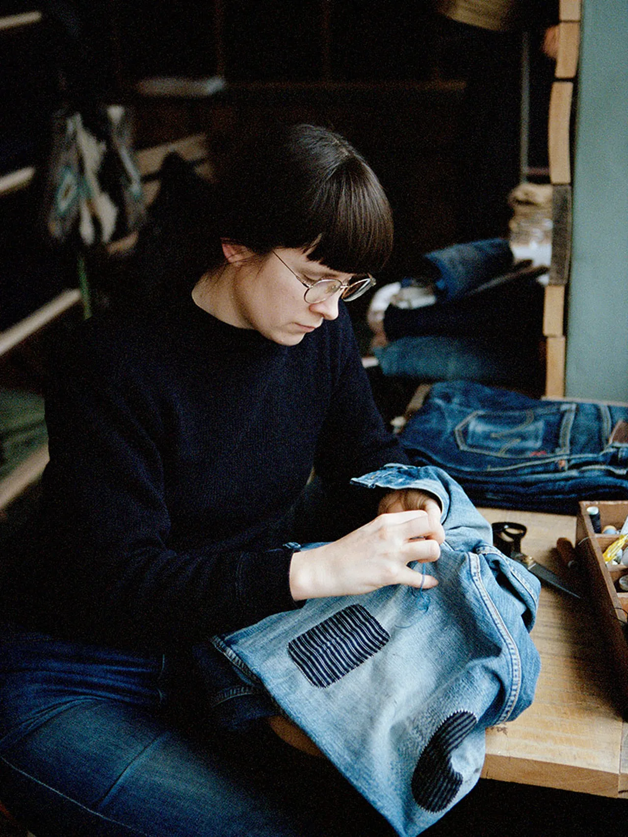 Tailor mending denim by hand in a workshop.